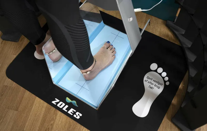 ZOLES 3D foot scanning station with person standing on illuminated blue scanning platform, showing the professional scanning equipment used at physiotherapy clinics